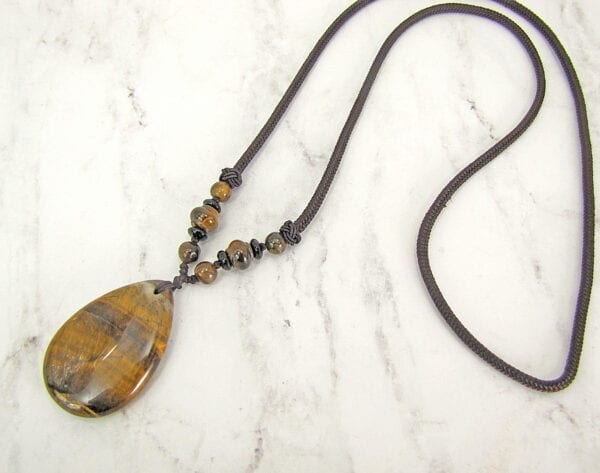 necklace pendant with banded brown gemstone on a marble surface