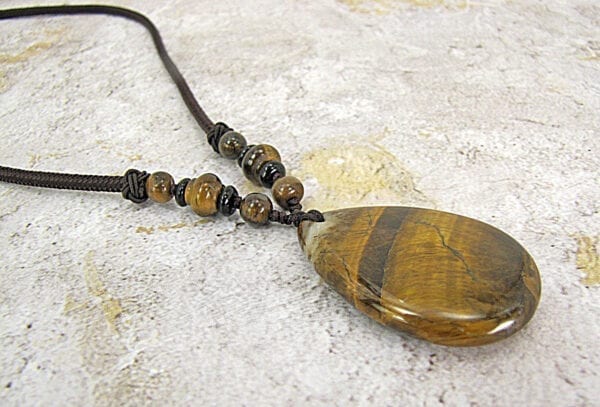 necklace pendant with banded brown gemstone on a concrete surface