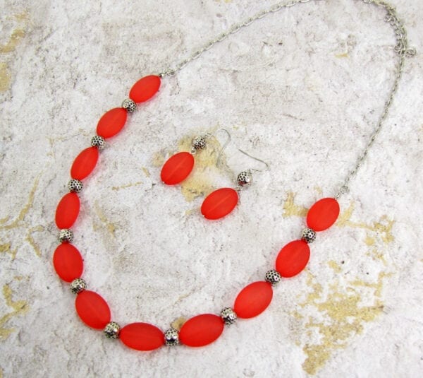 necklace and earrings with large red oval beads on a concrete surface