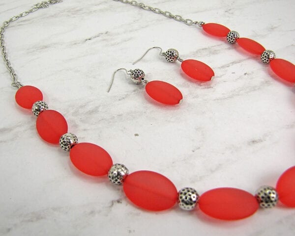 close up necklace and earrings with large red oval beads on a marble surface