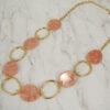 golden necklace with large hoops and pink beads on a marble surface