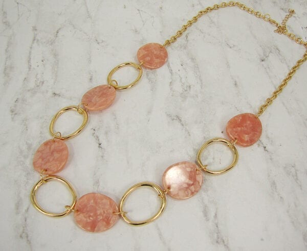 golden necklace with large hoops and pink beads on a marble surface
