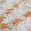 golden necklace with large hoops and pink beads on a textured surface