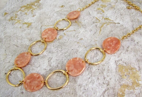golden necklace with large hoops and pink beads on a textured surface