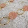 close up of a golden necklace with large hoops and pink beads on a textured surface
