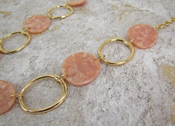 close up of a golden necklace with large hoops and pink beads on a textured surface