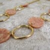 close up of a golden necklace with large hoops and pink beads on a concrete surface