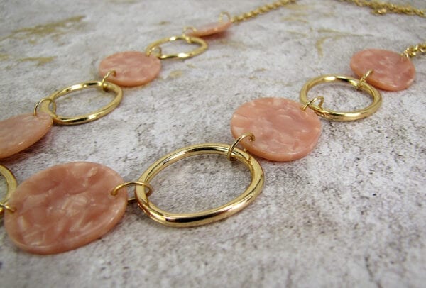 close up of a golden necklace with large hoops and pink beads on a concrete surface