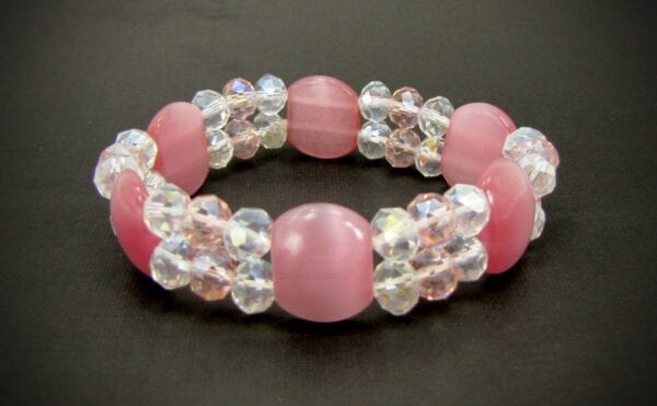 close up of a bracelet with pink stones and crystals on a black surface
